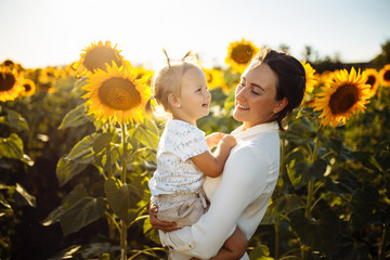 Young mother and her little daughter having fun and enjoy life at the sunflower field on a bright...