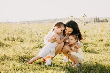 Mother and two daughters sitting outdoors in an open field with green grass.
