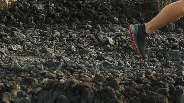 Close-up legs view. Young male athlete trail running on lava stones in mountains at 

sunrise. Sprain ligament or Achilles tendonitis. Healthy lifestyle concept.