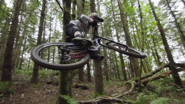 Experienced downhill mountainbiker performing classic whip on dirt feature, slow