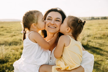 Mother and two daughters playing outdoors in a field. Girls kissing mother on cheeks.