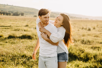 Young couple hugging and laughing outdoors in an open field on summer day.