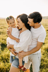 Mother, father and daughter in an open field, hugging and laughing.