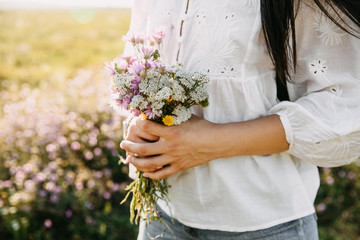 Closeup of a woman in an open field on a summer day holding a bouquet of wildflowers.