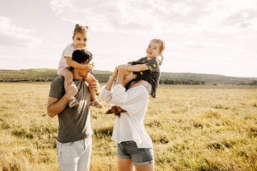 Family of four playing in a field on a summer day. Peek-a-boo game.