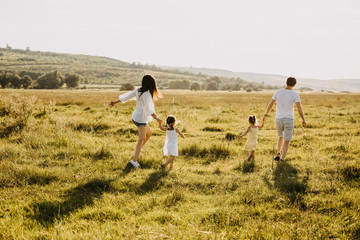 Family of four playing in an open field on a summer day, running on green grass.