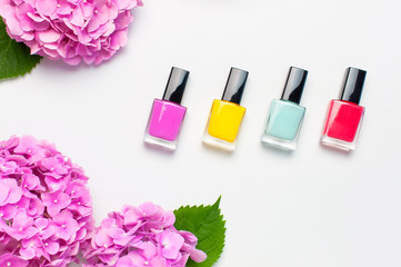 Obraz na płótnie Canvas Nail polish, Decorative cosmetics. Set of different varnishes for manicure nails on light background with flowers of pink hydrangea top view Flat lay mock up. Female cosmetics. Beauty blogger concept