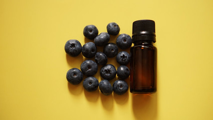 A bottle of blueberry seed essential oil and fresh blueberries on yellow background