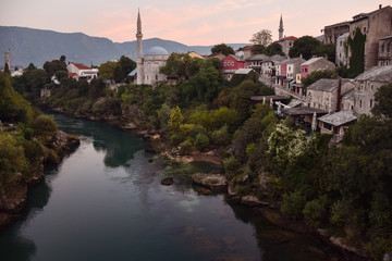 Fototapeta na wymiar Mostar village with mosque and houses reflected on the water of river during sunset time