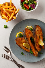 Fried carp in pieces, served on a gray plate. Marbled bright background.