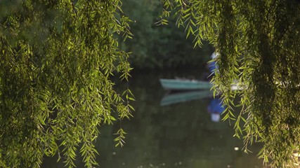 Blurry defocused silhouette of mature active woman sitting in wooden vintage boat rowing with paddle in river water. Happy senior person relaxing in scenic summer countryside landscape going to fish. - Powered by Adobe