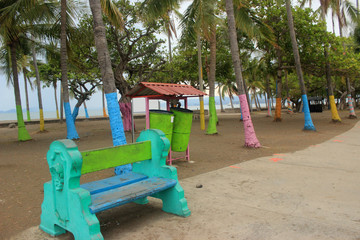 Colourful bench in front seaside path, bins and palm trees painted in various colours