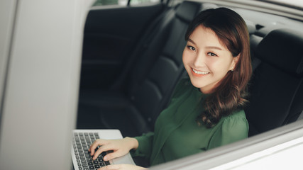 Beautiful businesswoman using laptop while sitting on a backseat of a car.