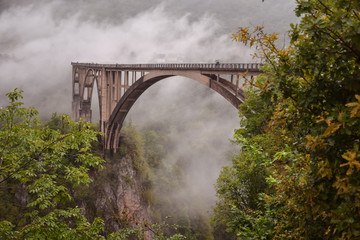 beautiful landscape of the arched bridge at river Piva near Mratinje dam with clouds and tourists watching scenery
