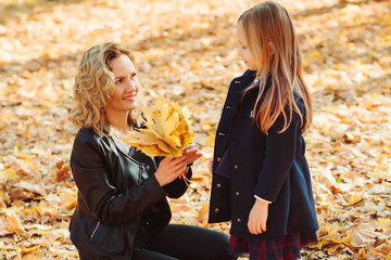 Mother and daughter walking in autumn park. Mom and child playing with autumn leaves.
