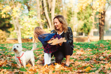 Mother and daughter having fun together outdoors. Fashionable mother and schoolgirl walking with their dog in park.