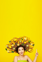 Obraz na płótnie Canvas beautiful girl lying on yellow background with citrus fruits in long hair,young woman shows direction finger up,advertising sale