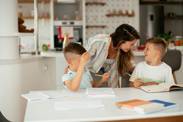 Mother helping her sons with homework at home. Little boys learning at home..