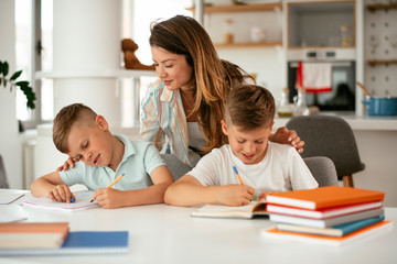 Mother helping her sons with homework at home. Little boys learning at home..