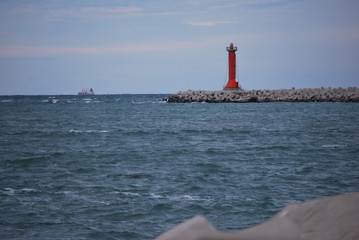 
red lighthouse marking the harbor dam to ships in transit with ship in the background