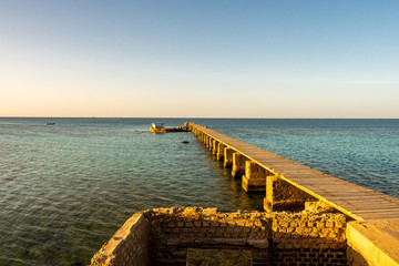Old wooden pier (jetty) of the Sanganeb Reef Lighthouse near Port Sudan, on the Red Sea, in Sanganeb National Park, with endless horizon sea view during golden hour sunset.