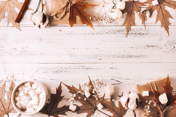 Cup of  cocoa with marshmallows, hot chocolate,  autumn yellow maple leaves, cones, cinnamon sticks, a gift box, a sprig of white flowers and cotton on a white wooden ,  copy space
