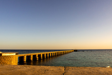 Old wooden pier (jetty) of the Sanganeb Reef Lighthouse near Port Sudan, on the Red Sea, in Sanganeb National Park, with endless horizon sea view during golden hour sunset, purple sky. Low horizon.