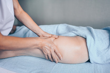 Young unrecognizable woman lying on massage table and enjoying therapeutic massage. Body care, losing weight concept. Hands masseur massage therapist doing anti-cellulite massage in spa clinic.