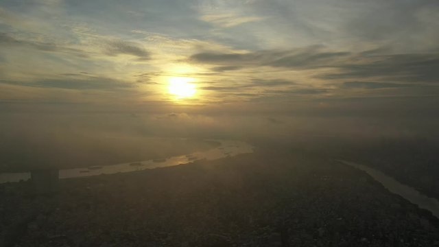 Early morning urban drone flight tracking right between Saigon river with heavy shipping and canal over populated area of Ho Chi Minh City with heavy fog and low clouds