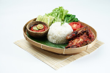Spicy grilled chicken with ripe red skin laid out on a wooden sheet on a white background, plus white rice, chili sauce and various vegetables, view from above. commonly used for menus and box wrap im