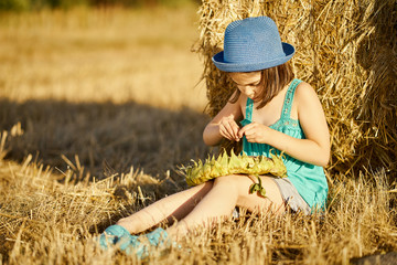 adorable girl eating sunflower seeds on mown rye in the field