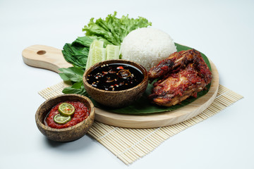 Spicy grilled chicken with ripe red skin laid out on a wooden sheet on a white background, plus white rice, chili sauce and various vegetables, view from above. commonly used for menus and picture pac
