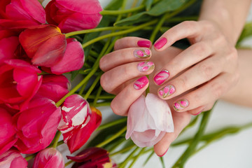 Obraz na płótnie Canvas Female hands with tender spring manicure holding pink fresh tulip on flowers background. Nail art, gel nails polish design and beauty concept.