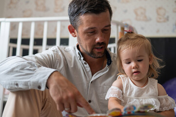 Obraz premium A caring father reads a fairy tale to his little daughter in the children's bedroom.