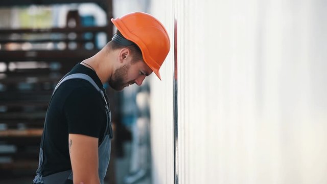 Stressed employee in orange hard hat knocks his head against the wall.