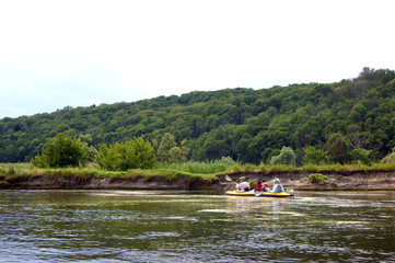 Family rowing in a yellow kayak in summer along the trees at the bank of Seversky Donets river.