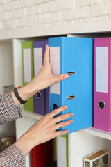 Multicolored folders in the office, a woman takes a folder of documents from the closet