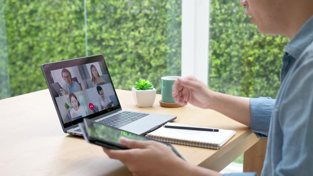 Slow motion zoom in back view : business man talking in video conference.Asian team using laptop and tablet online meeting in video call.Working from home, Working remotely and Self isolation at home