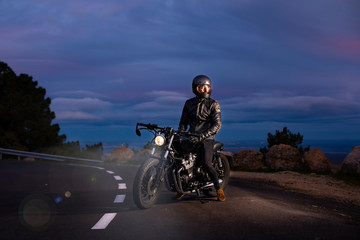Rider with black cuscom motorcycle on the road at dusk