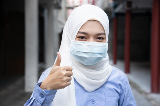 Muslim woman suggesting to wearing face mask in outdoor public with thumb up gesture; concept of new normal lifestyle, social distancing, flatten the curve, preventive measure against flu pandemic