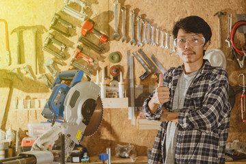 Portrait of asian craftsman with equipment standing in workshop and looking at camera. Carpenter in...