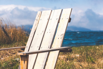 Fototapeta premium Wooden chair on the beach of a relaxing lake at sunrise