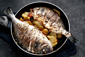 fried dorado fish and potatoes in a frying pan on a stone background