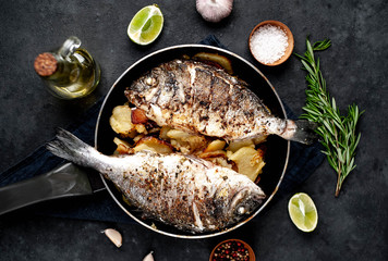 fried dorado fish and potatoes in a frying pan on a stone background
