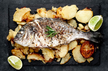 fried dorado fish and potatoes with ingredients on stone background