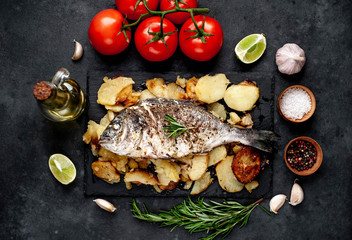 fried dorado fish and potatoes with ingredients on stone background