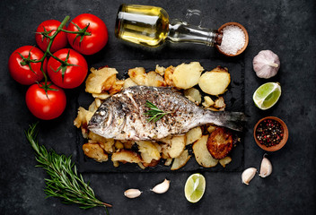 fried dorado fish and potatoes with ingredients on stone background