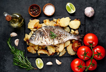 fried dorado fish and potatoes with ingredients on stone background