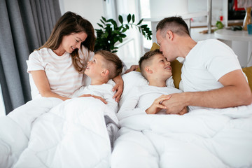 Obraz premium Young family enjoying in bed. Happy parents with sons relaxing in bed..