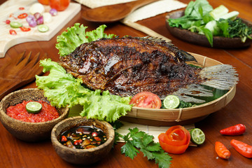 photos of food products, View from above Close up of grilled fish or grilled gouramy with chili sauce and vegetables on a textured wooden table. Usually used for menu list pictures or food pictures in